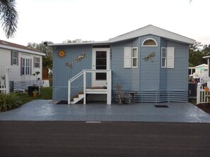 Einbungalow mit Veranda, einer kleinen Treppe und dekorativen Elementen wie einer Sonne und einem Vogel.