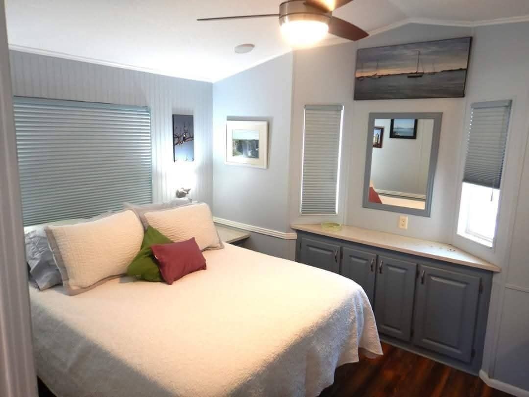 A bedroom with a bed, a ceiling fan, a window with blinds, and a mirror on the wall.