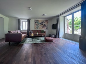 Ein geräumiges Wohnzimmer mit Holzboden, einer Couch, einem Couchtisch und einem Fernseher.