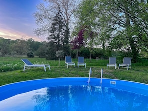 Piscina com quatro espreguiçadeiras e uma árvore ao fundo.