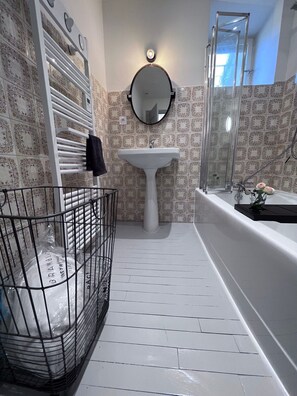 Um banheiro com pia branca, espelho redondo, chuveiro e parede revestida com azulejos.
