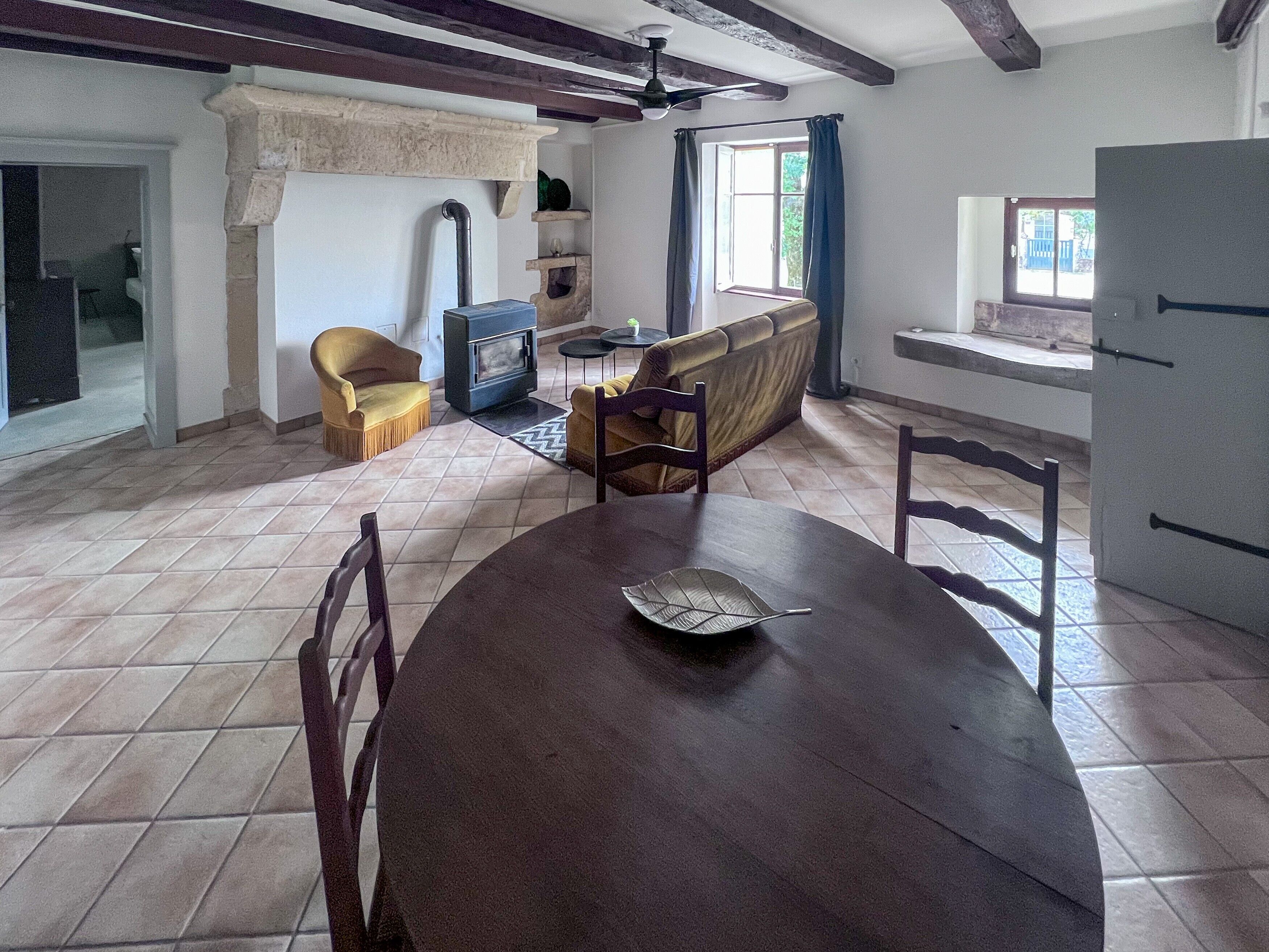 A dining area with a wooden table and chairs, a sofa, a fireplace, and a window with curtains.