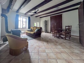 Ein Wohnzimmer mit einer Couch, einem Esstisch mit Stühlen, einem Deckenventilator und einer Küchenzeile mit Schränken.