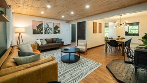 A modern living room with a wooden ceiling, a sofa, a coffee table, and a dining area with chairs and a table. - Moonstone | Hocking Hills, Modern, Hot Tub (Rockbridge)