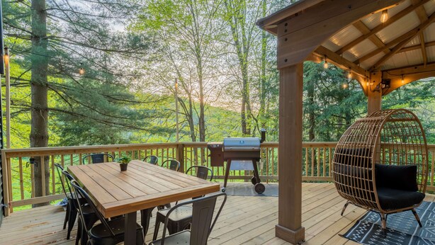 A wooden deck with a table and chairs, a grill, and a hanging chair. - Moonstone | Hocking Hills, Modern, Hot Tub (Rockbridge)