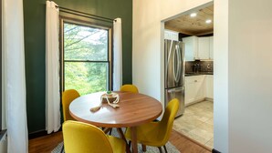 A dining area with a round table, yellow chairs, a window with curtains, and a kitchen with white cabinets and stainless steel appliances. - Moonstone | Hocking Hills, Modern, Hot Tub (Rockbridge)