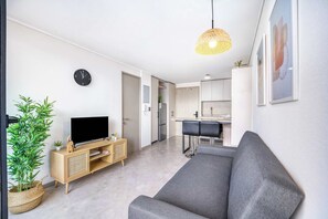A modern living room with a grey sofa, a flat-screen TV, a wooden cabinet, and a large potted plant. - The Place Apartment 1BR and Wifi (Ñuñoa)