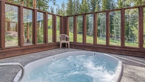 Ein Whirlpool mit Blick auf einen Wald, umgeben von Holzwänden mit großen Fenstern.