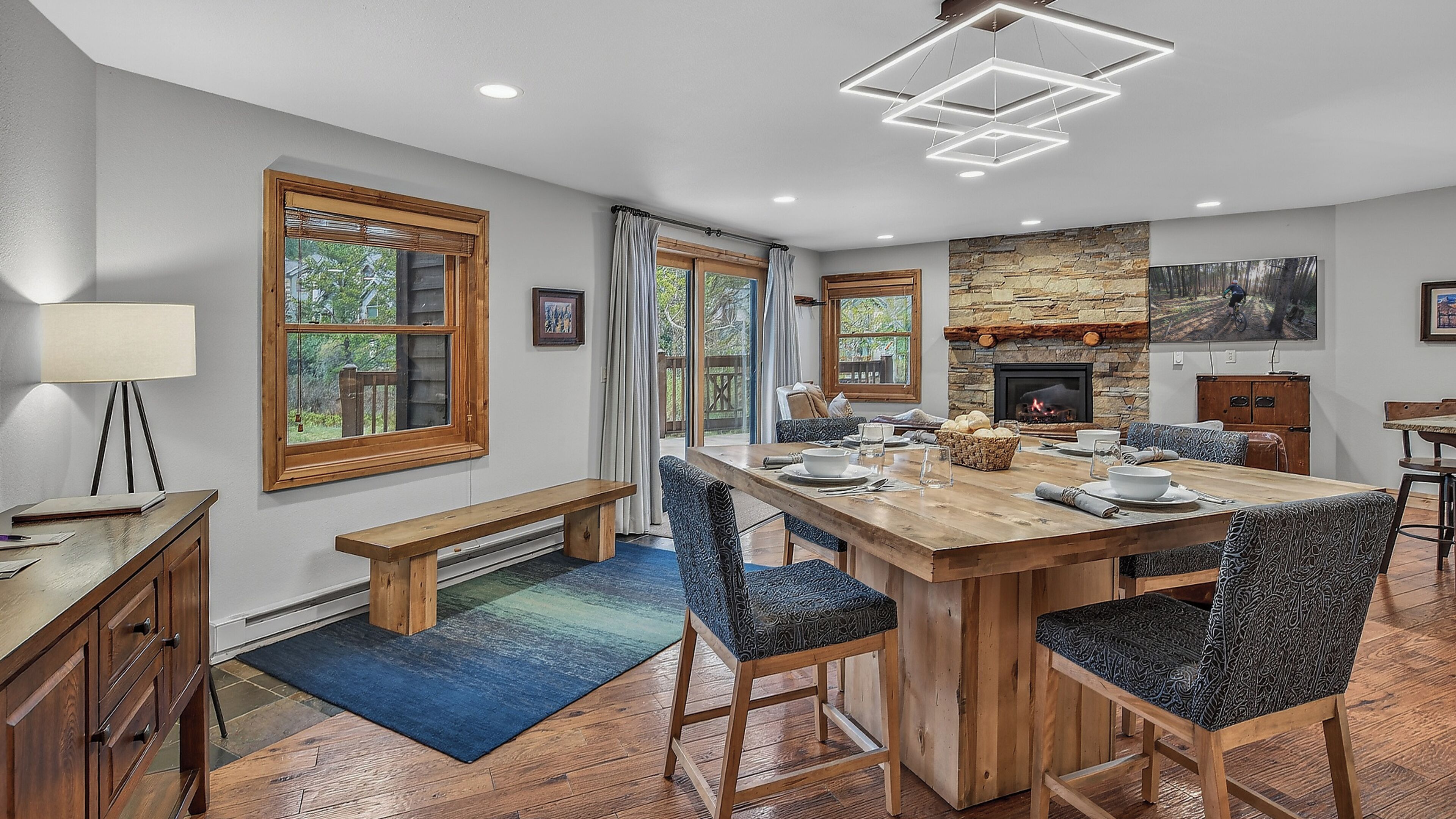 A dining area with a wooden table, chairs, a bench, a fireplace, and a view of the outdoors.