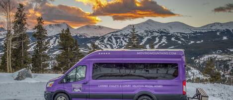 A purple moving van parked on a snowy road with mountains in the background.