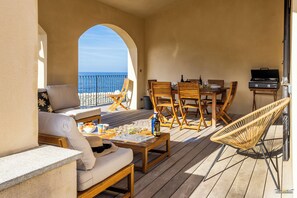 Eine Terrasse mit Holzmöbeln, einem Grill und Blick aufs Meer.