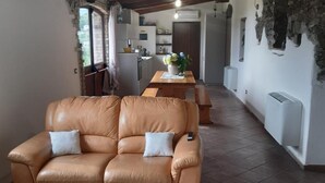 Un salon chaleureux avec un canapé en cuir, une table à manger avec des chaises, et une cuisine en arrière-plan.