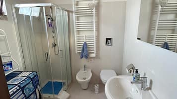 Uma casa de banho com chuveiro em cabine de vidro, bidé, sanita, lavatório e espelho.
