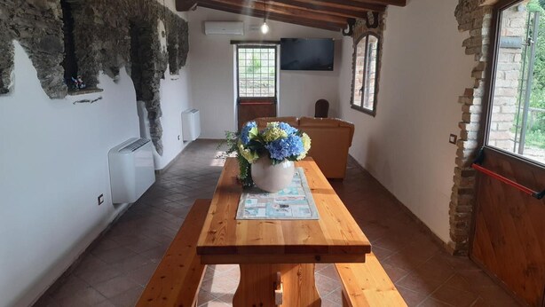 Un coin repas rustique avec une table en bois, des bancs, un vase de fleurs et un téléviseur fixé au mur.