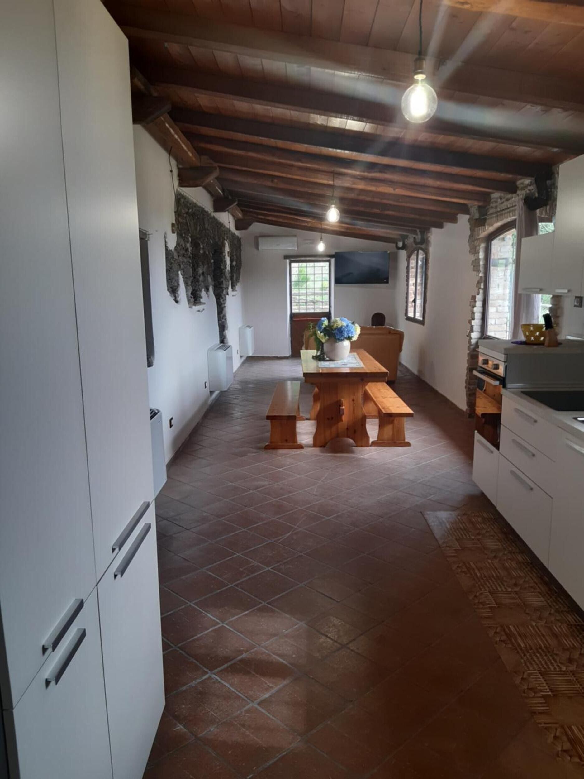 Une cuisine avec des meubles blancs, un banc en bois et un sol carrelé.