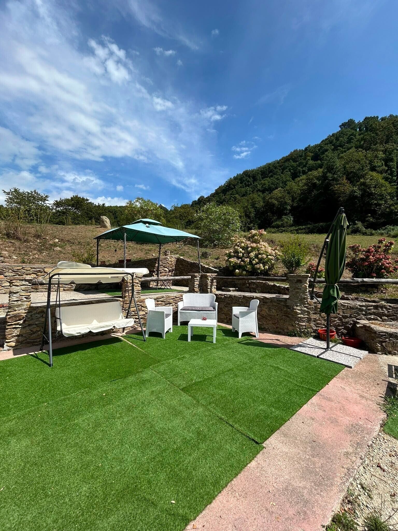 Un espacio al aire libre con césped artificial, paredes de piedra y mobiliario exterior.