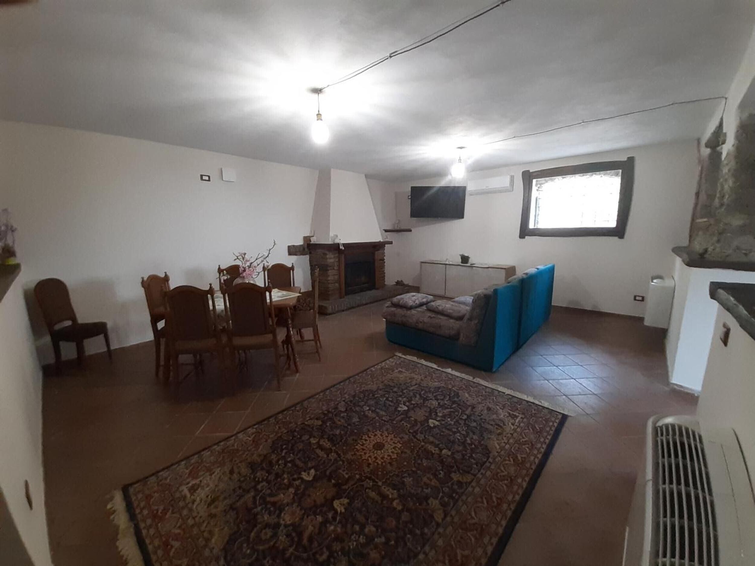 Una sala de estar con chimenea, un televisor montado en la pared, una mesa de comedor con sillas y un sofá azul.