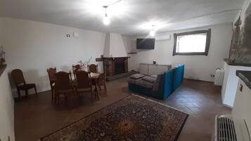 Una sala de estar con chimenea, un televisor montado en la pared, una mesa de comedor con sillas y un sofá azul.