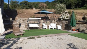 Une terrasse extérieure avec des murs en pierre, un espace barbecue et une pelouse verdoyante.