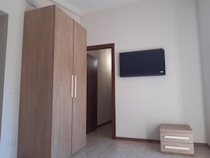 Ein Zimmer mit Kleiderschrank, Flachbildfernseher und einem kleinen Nachttisch.