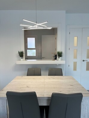A modern dining area with a wooden table, four chairs, a pendant light, and a view into a kitchen through a doorway. - Cozy apartment near the beach with a private terrace and a shared pool (San José)
