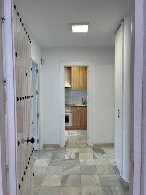 A hallway leading to a kitchen with a tiled floor, wooden cabinets, and a white door with a handle. - Cozy apartment near the beach with a private terrace and a shared pool (San José)