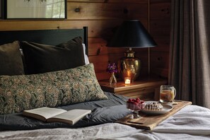 Een knus slaapkamer met een bed, kussens, een nachtkastje met een lamp, een glas thee en een bord met aardbeien.