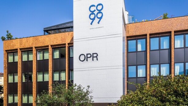 Un bâtiment moderne avec une enseigne bien visible indiquant « CO 99 HOTEL & RESIDENCE » et « OPR » sur la façade.
