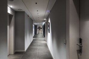 A modern hotel corridor with a long, straight path, recessed lighting, and a door with a keypad lock. - CO99 - DYNAMIC ROOM (Milano)