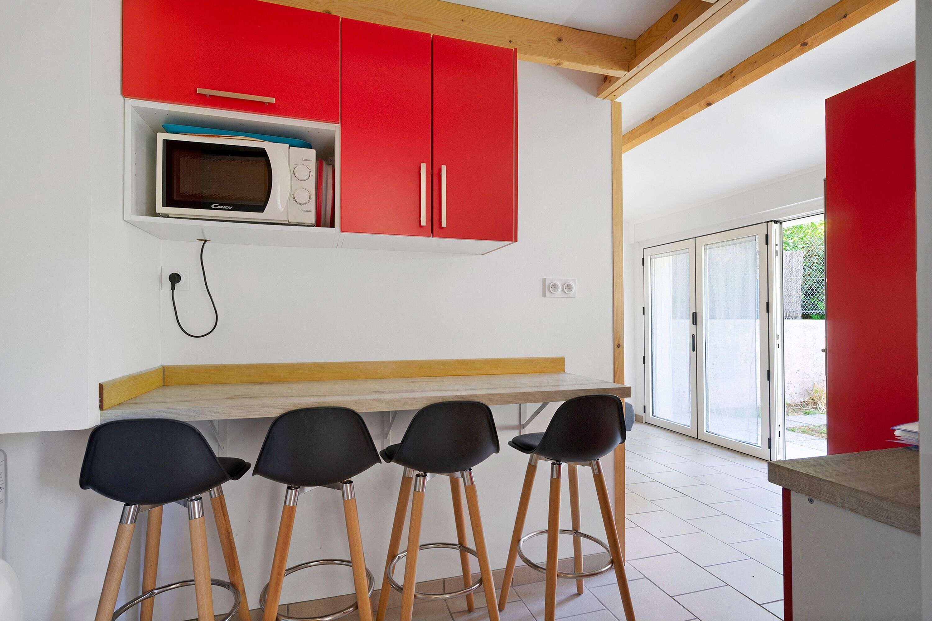 Une cuisine équipée d’un four à micro-ondes, de placards rouges et d’un coin bar avec des tabourets.