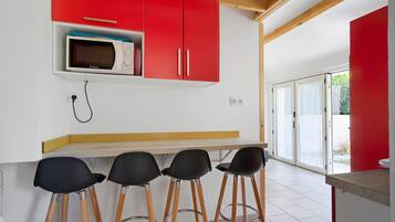 Une cuisine équipée d’un four à micro-ondes, de placards rouges et d’un coin bar avec des tabourets.