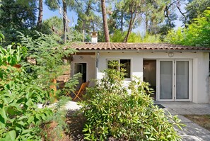 Une maison avec un toit en tuiles, un petit porche et un jardin où poussent différentes espèces de plantes.