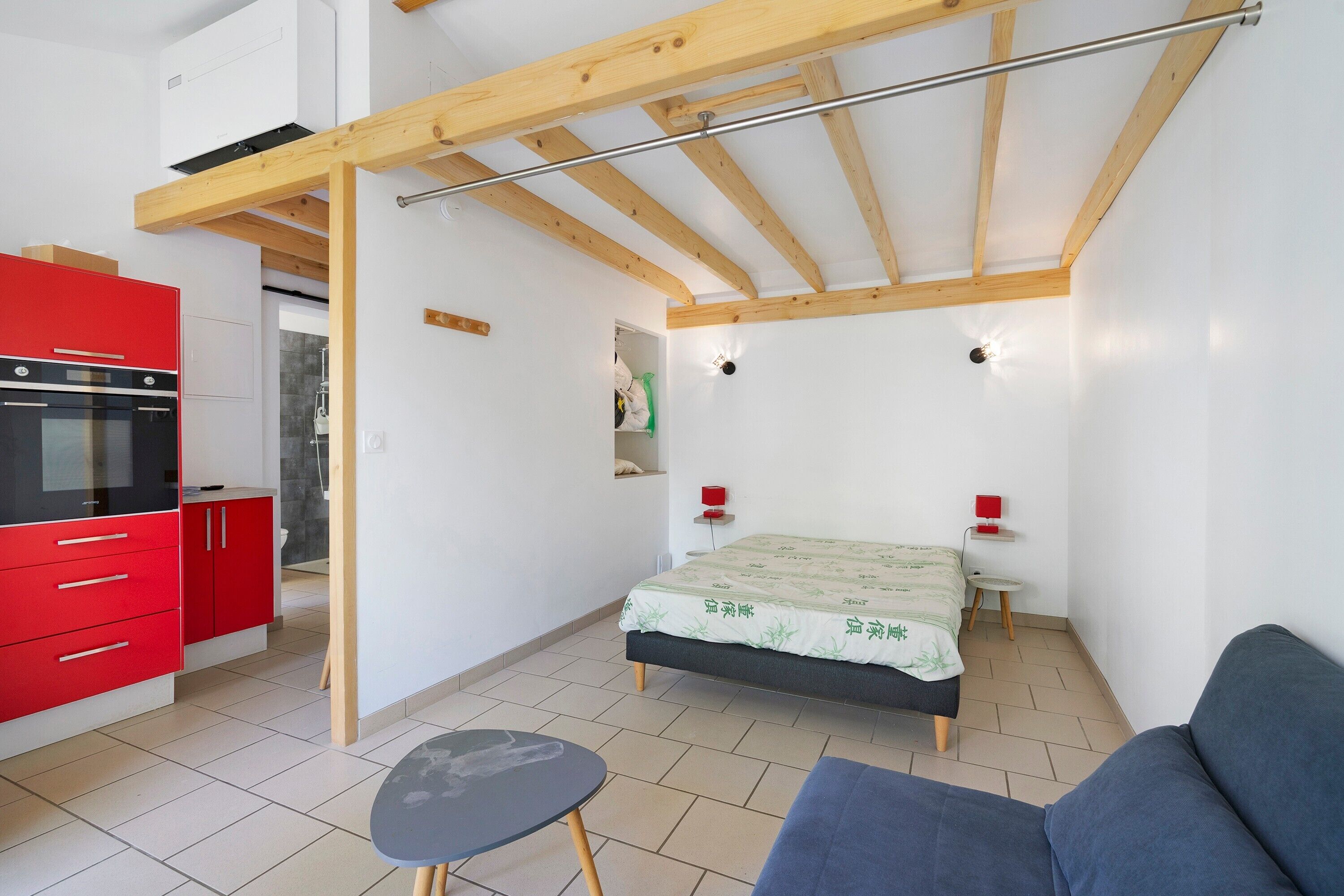A compact room with a kitchenette, a bed, a small table, and a sofa.