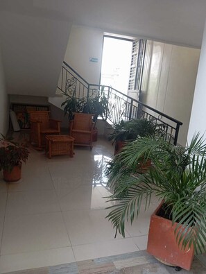 A spacious indoor area with a staircase, wicker furniture, and potted plants.