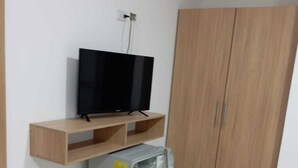 A room with a television on a wooden shelf, a refrigerator, and a wooden wardrobe. - Hotel Casa Grande  (Agustín Codazzi)