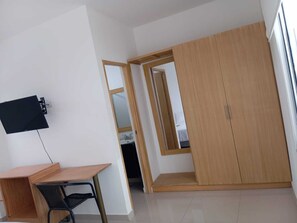 A room with a desk, chair, wardrobe, and a TV mounted on the wall.