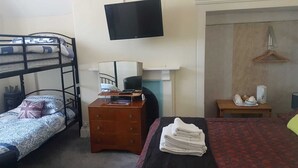 Une chambre de dortoir avec des lits superposés, un bureau avec un ordinateur, une télévision et une petite table avec une bouilloire.