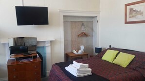 Une chambre à coucher avec un lit, une télévision, un bureau avec un ordinateur et une cheminée.