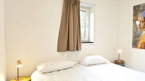 Ein Schlafzimmer mit einem Bett, zwei Nachttischen, einem Fenster mit Vorhängen und einem Wandbild.