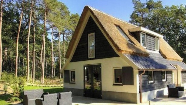Ein zweistöckiges Haus mit Strohdach, einer Terrasse mit Gartenmöbeln und einem angelegten Garten.