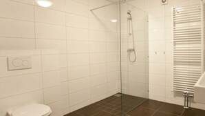 Ein Badezimmer mit weißen Fliesen, einer Glasdusche, einer weißen Toilette und einem Handtuchhalter.