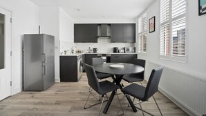 A modern kitchen with a central island, dark cabinetry, and a dining area with a round table and chairs. - Modern Luxury 2-Bedroom Apartment with Roof Terrace & Fast Wi-Fi (Isleworth)