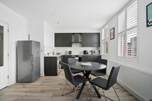 Eine moderne Küche mit Kochinsel, dunklen Schränken und einem Essbereich mit rundem Tisch und Stühlen.