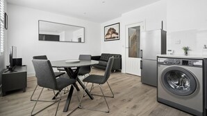 A modern kitchen with a built-in washing machine, a dining area with a round table and chairs, and a large mirror on the wall. - Modern Luxury 2-Bedroom Apartment with Roof Terrace & Fast Wi-Fi (Isleworth)