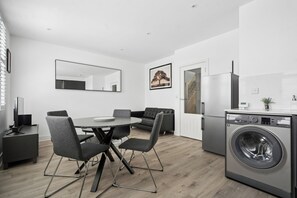 Eine moderne Küche mit Einbauwaschmaschine, einem Essbereich mit rundem Tisch und Stühlen sowie einem großen Spiegel an der Wand.