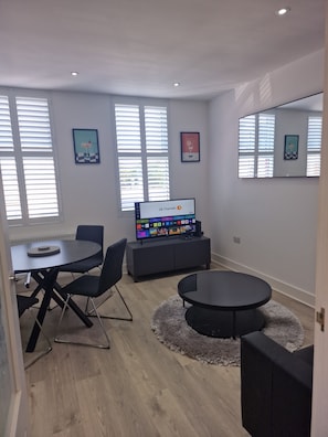 Een moderne woonkamer met een flatscreen televisie, een eettafel met stoelen, een bank en een grote spiegel.