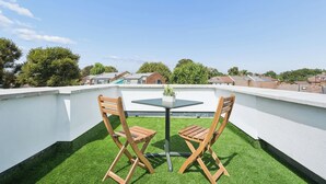 A rooftop terrace with a small table and two wooden chairs, surrounded by artificial grass. - Modern Luxury 2-Bedroom Apartment with Roof Terrace & Fast Wi-Fi (Isleworth)