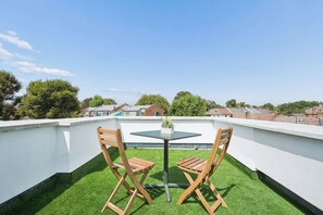Eine Dachterrasse mit einem kleinen Tisch und zwei Holzstühlen, umgeben von Kunstgrün.