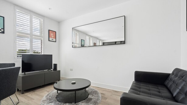 A modern living room with a flat-screen TV, grey sofa, round coffee table, and a large mirror on the wall. - Modern Luxury 2-Bedroom Apartment with Roof Terrace & Fast Wi-Fi (Isleworth)
