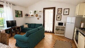 A living room with a sofa, TV, and kitchen area with a fridge and microwave. - Villa Fiammetta, 500 meters from the beach (Castiadas)